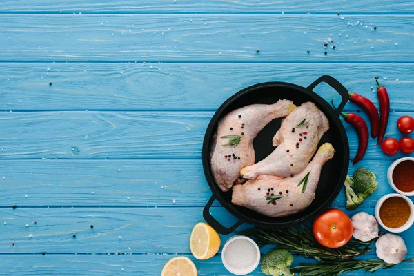 Vista superior de patas de pavo crudo en sartén con diferentes verduras en la mesa azul - foto de stock