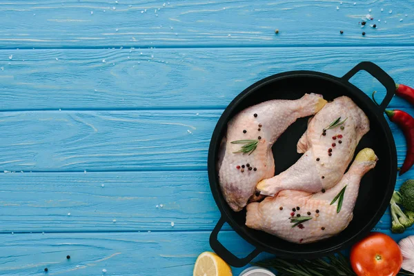 Vue du dessus des cuisses de poulet dans une casserole et différents légumes et épices sur plateau en bois bleu — Photo de stock
