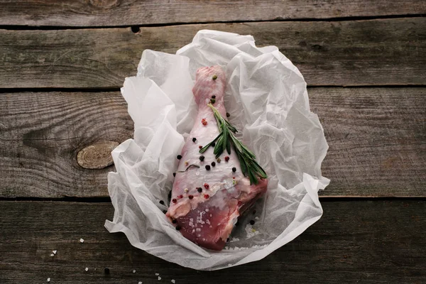 Uncooked turkey leg with pepper corns and rosemary on baking paper on wooden tabletop — Stock Photo