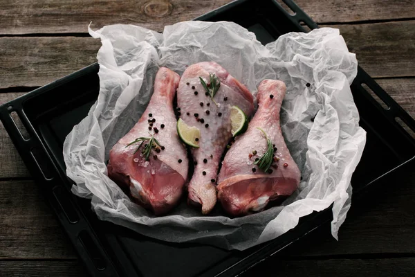 Unprocessed turkey legs with pepper corns, rosemary and lime on baking paper on dish — Stock Photo