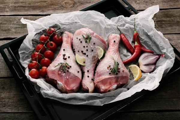 Raw chicken legs with spices and fresh vegetables on paper on baking dish — Stock Photo
