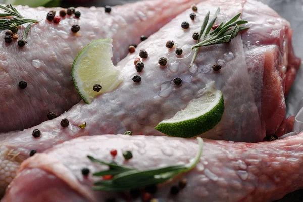 Vista de perto de pernas de frango crus com grãos de pimenta, alecrim e limão — Fotografia de Stock