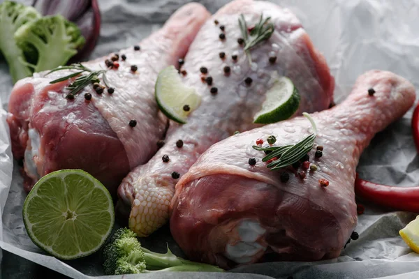 Patas de pavo sin cocer con granos de pimienta, romero y lima sobre papel de hornear - foto de stock