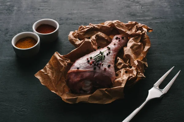 Raw turkey leg with pepper corns on baking paper on wooden table with paprika spices — Stock Photo