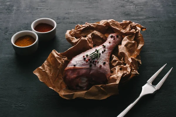 Jambe de dinde crue avec des grains de poivre sur papier cuisson sur table en bois avec des épices au paprika — Photo de stock