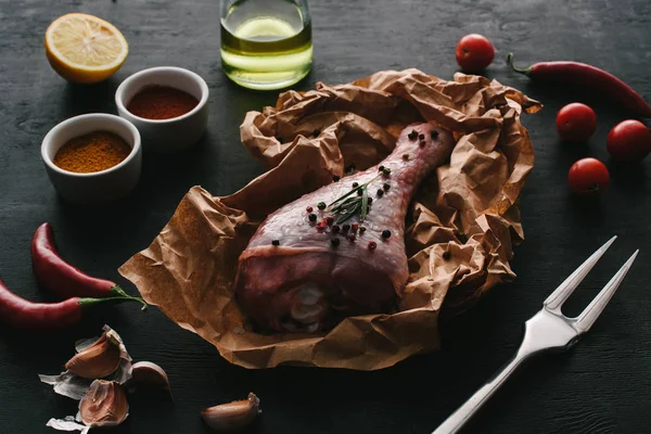 Una coscia di tacchino con grani di pepe su carta da forno su un tavolo di legno con verdure e spezie — Foto stock