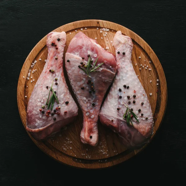 Vue du dessus des cuisses de dinde crue avec des grains de poivre et du romarin sur planche à découper en bois — Photo de stock