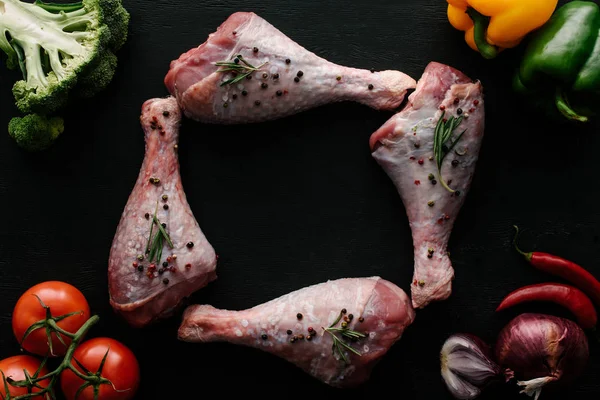 Top view of raw turkey legs with pepper corns, rosemary and different vegetables on wooden black table — Stock Photo