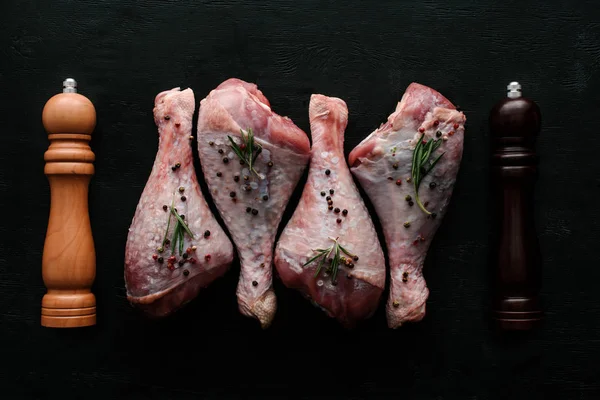 Vista superior de pernas de frango cru com grãos de pimenta e alecrim em mesa de madeira com pimenta e saladeira — Fotografia de Stock