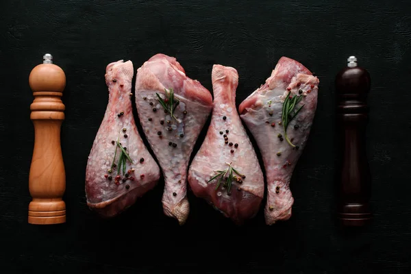 Ansicht von rohen Hühnerkeulen mit Pfefferkörnern und Rosmarin auf hölzerner Tischplatte mit Pfeffer und Salzkeller — Stockfoto