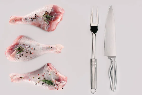 Vista dall'alto di cosce di pollo con grani di pepe, rosmarino, forchetta e coltello, isolato su bianco — Foto stock