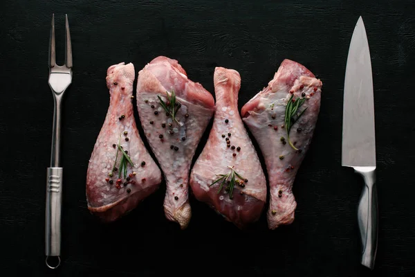 Vue du dessus des cuisses de poulet avec des grains de poivre et du romarin sur table noire — Photo de stock