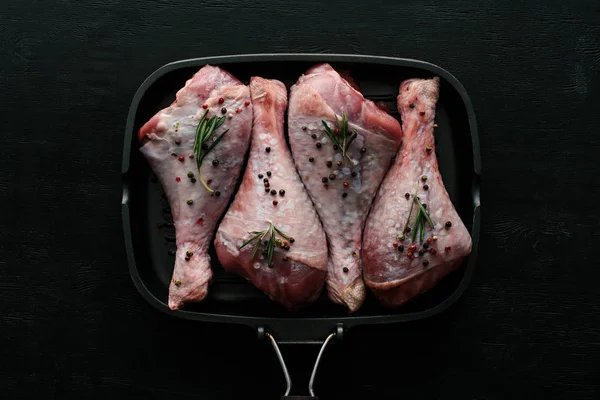 Top view of chicken legs with pepper corns and rosemary in grill pan on black wooden table — Stock Photo