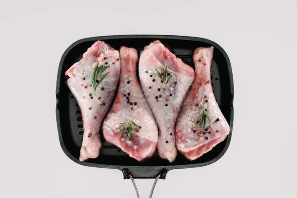 Верхний вид куриные ножки с перцем мозоли, розмарин и соль на сковороде гриль, изолированные на белом — стоковое фото