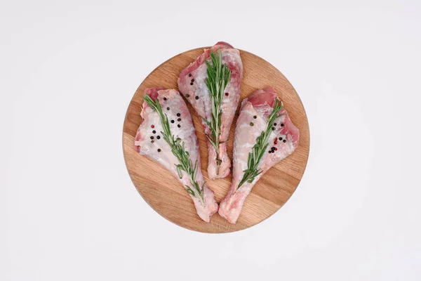 Top view of raw chicken legs with pepper corns and rosemary on wooden cutting board, isolated on white — Stock Photo