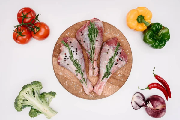 Top view of uncooked chicken legs with rosemary on cutting board with raw vegetables near, isolated on white — Stock Photo