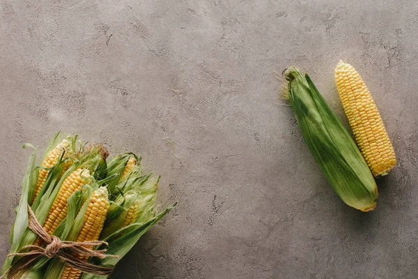 Draufsicht auf frische Maiskolben, die mit Seil und einem Mais auf grauer Betonoberfläche auseinander gebunden sind — Stockfoto