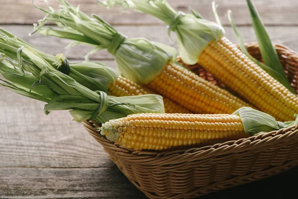 Vista de cerca de mazorcas de maíz crudo en la cesta en la superficie de madera - foto de stock