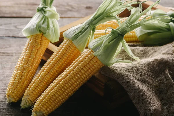 Nahaufnahme von reifen Maiskolben in Schachtel mit Sacktuch auf Holzoberfläche — Stockfoto