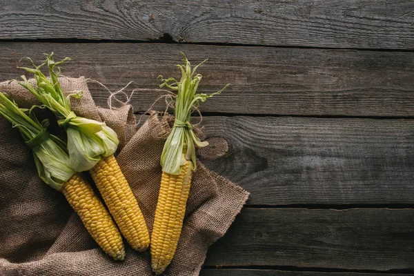 Draufsicht auf frische rohe Maiskolben auf Sacktuch auf hölzerner Tischplatte — Stockfoto