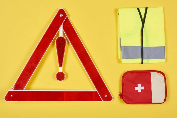 Vista superior de la señal de carretera triángulo de advertencia, botiquín de primeros auxilios y chaleco reflectante aislado en amarillo - foto de stock