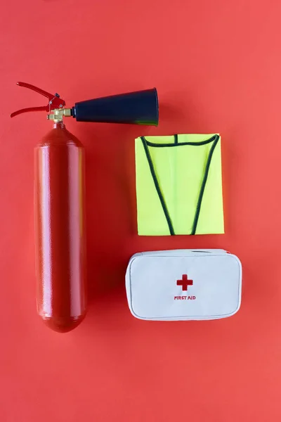 Vista superior do extintor de incêndio, colete reflexivo e kit de primeiros socorros no fundo vermelho — Fotografia de Stock