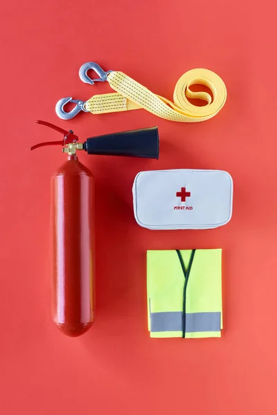Feuerlöscher, Abschleppseil, Warnweste und Verbandskasten auf rotem Hintergrund — Stockfoto