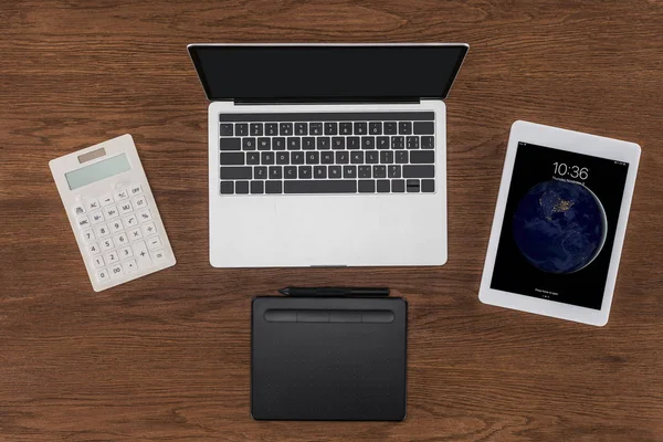 Vue du dessus de l'ordinateur portable avec écran vierge, calculatrice, manuel et tablette ipad sur table en bois — Photo de stock