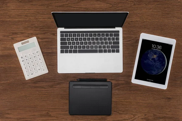 Top view of laptop with blank screen, calculator, textbook and ipad tablet on wooden table — Stock Photo