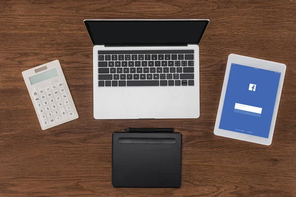 Top view of laptop with blank screen, calculator, textbook and digital tablet with facebook on screen — Stock Photo
