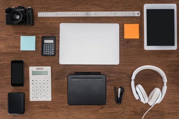 Top view of workplace with laptop, ruler, photo camera, smartphone and digital tablet on wooden table — Stock Photo