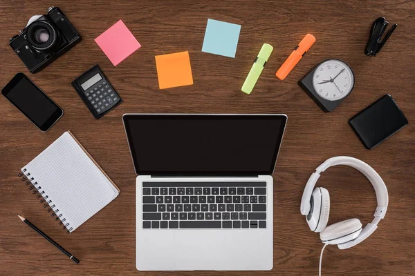 Top view of wooden table with empty textbook, smartphone, photo camera and laptop with blank screen — Stock Photo