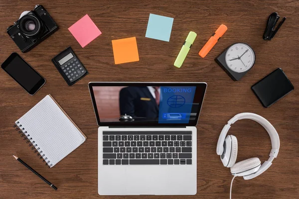 Draufsicht auf Holztisch mit leerem Lehrbuch, Smartphone, Fotokamera und Laptop mit Buchung auf dem Bildschirm — Stock Photo