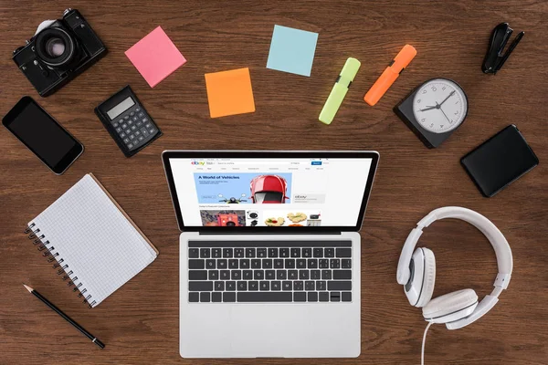 Draufsicht auf Holztisch mit leerem Lehrbuch, Smartphone, Fotokamera und Laptop mit ebay auf dem Bildschirm — Stock Photo