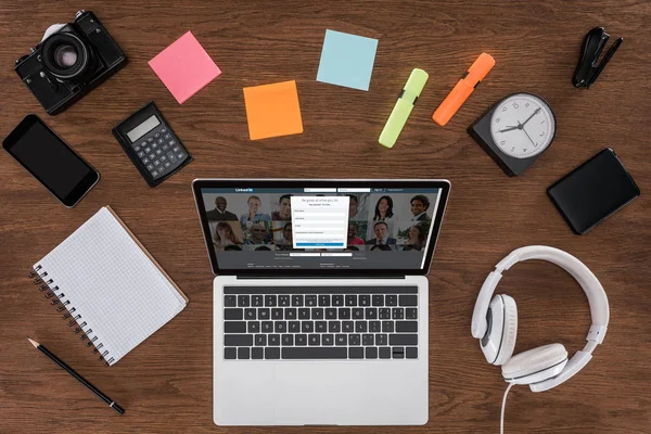 Draufsicht auf Holztisch mit leerem Lehrbuch, Smartphone, Fotokamera und Laptop mit Linkedin auf dem Bildschirm — Stock Photo