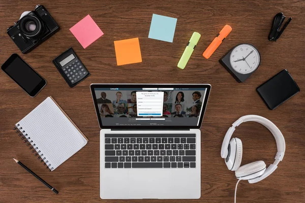 Top view of wooden table with empty textbook, smartphone, photo camera and laptop with linkedin on screen — Stock Photo