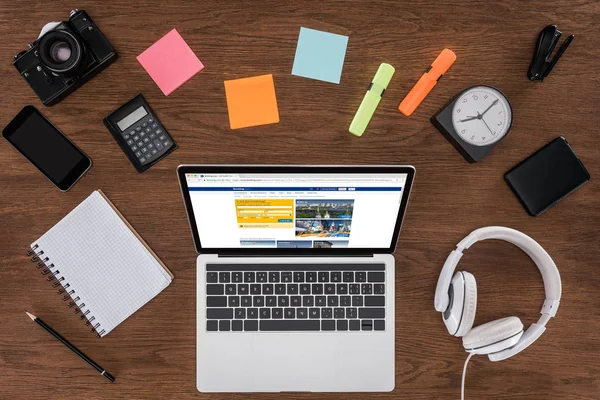 Top view of wooden table with empty textbook, smartphone, photo camera and laptop with booking.com on screen — Stock Photo