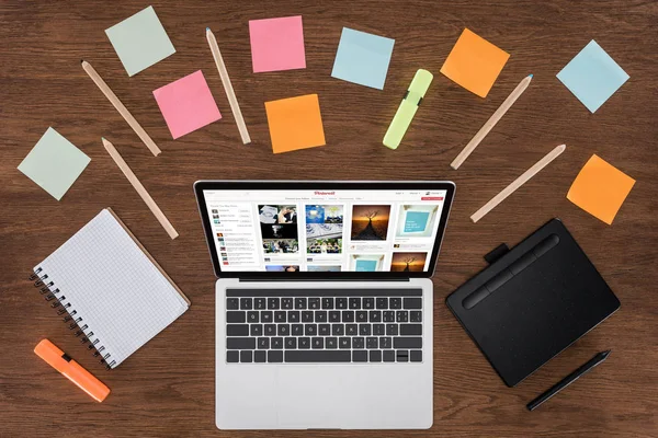 Top view of workplace with arranged textbooks, post it and laptop with pinterest on screen — Stock Photo