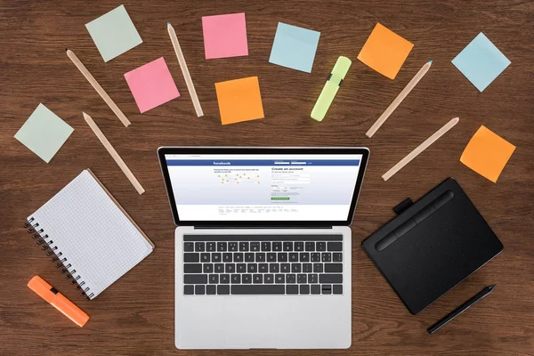 Top view of workplace with arranged textbooks, post it and laptop with facebook on screen — Stock Photo