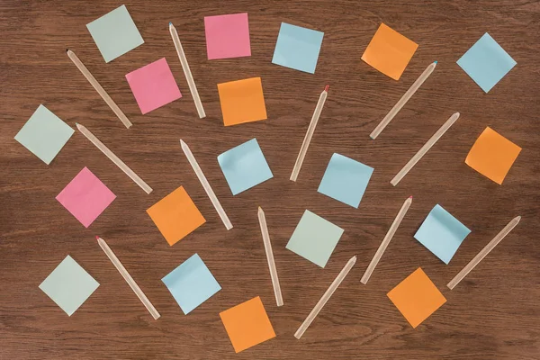 Draufsicht auf arrangierte bunte Post-it-Notizen und Bleistifte auf Holztisch — Stockfoto