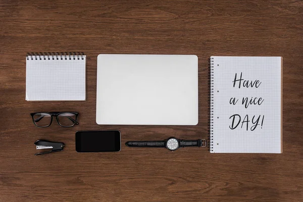 Vista superior del lugar de trabajo con ordenador portátil arreglado, reloj de pulsera, teléfono inteligente y libro de texto con letras tienen un buen día en la mesa de madera - foto de stock