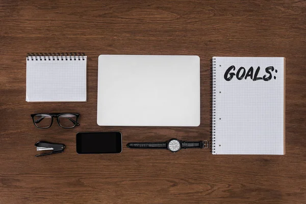 Top view of workplace with arranged laptop, wristwatch, smartphone and textbook with lettering goals on wooden table — Stock Photo