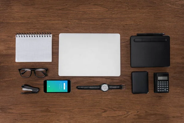 Top view of workplace with arranged empty textbook, laptop, wristwatch and smartphone with twitter on screen — Stock Photo