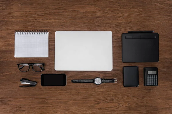 Vue du dessus du lieu de travail avec manuel vide arrangé, ordinateur portable, montre-bracelet et smartphone sur table en bois — Photo de stock