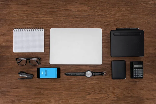 Top view of workplace with arranged empty textbook, laptop, wristwatch and smartphone with skype on screen — Stock Photo