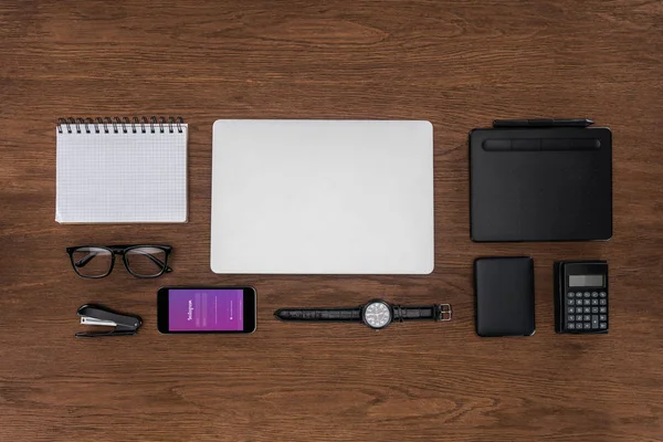 Vue du dessus du lieu de travail avec manuel vide arrangé, ordinateur portable, montre-bracelet et smartphone avec instagram à l'écran — Photo de stock