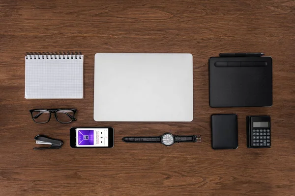 Ansicht des Arbeitsplatzes mit leerem Lehrbuch, Laptop, Armbanduhr und Smartphone mit Apple-Musikapplikation auf dem Bildschirm — Stockfoto