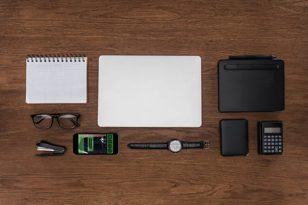 Top view of workplace with arranged empty textbook, laptop, wristwatch and smartphone with booking on screen — Stock Photo