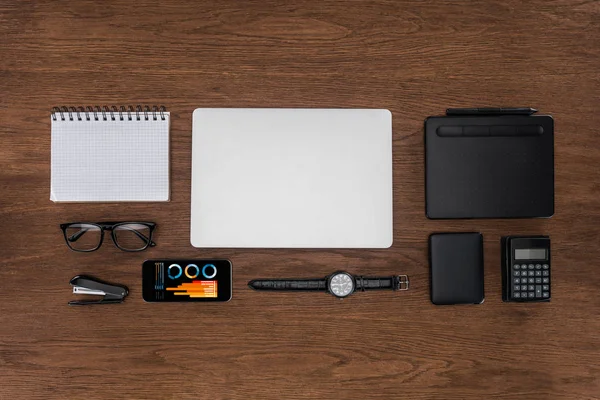 Top view of workplace with arranged empty textbook, laptop, wristwatch and smartphone with graphics on screen — Stock Photo