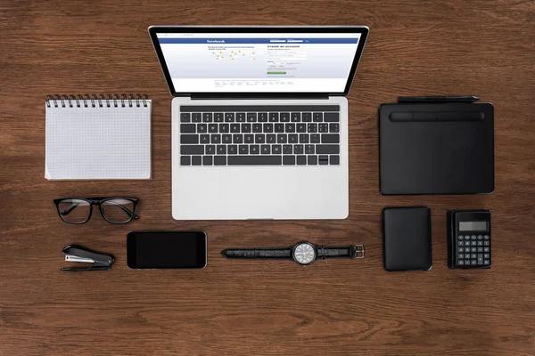 Top view of workplace with arranged empty textbook, smartphone, wristwatch and laptop with facebook on screen — Stock Photo